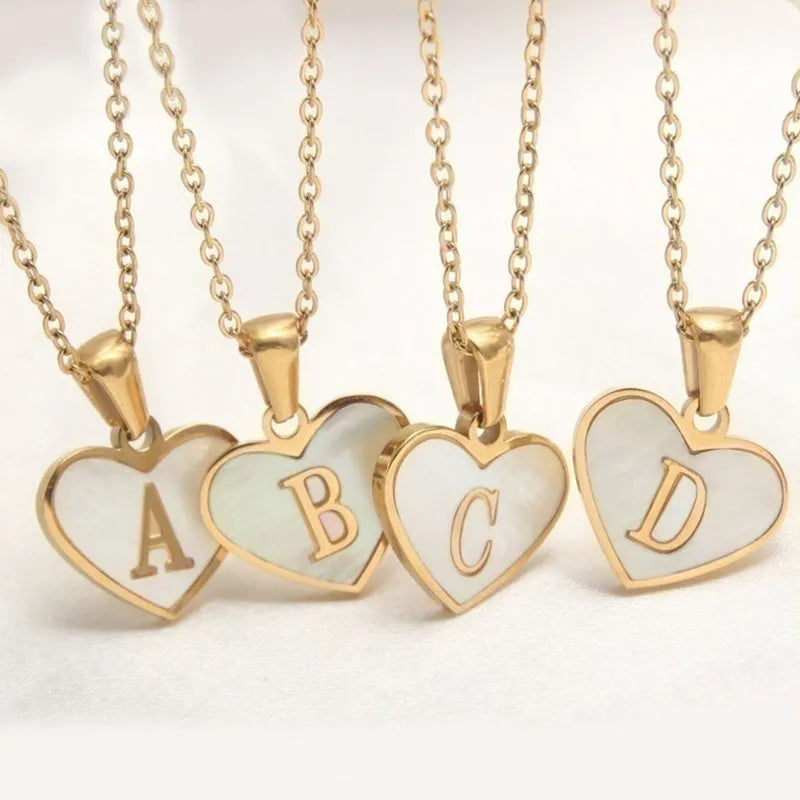 Gold-plated heart-shaped white shell initial necklace on a model, showing the adjustable clavicle chain.