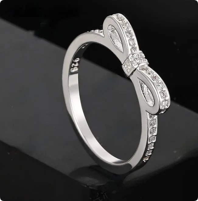 Silver bow-shaped ring with zircon crystal accents on finger, showing electroplated finish and detailed bow structure