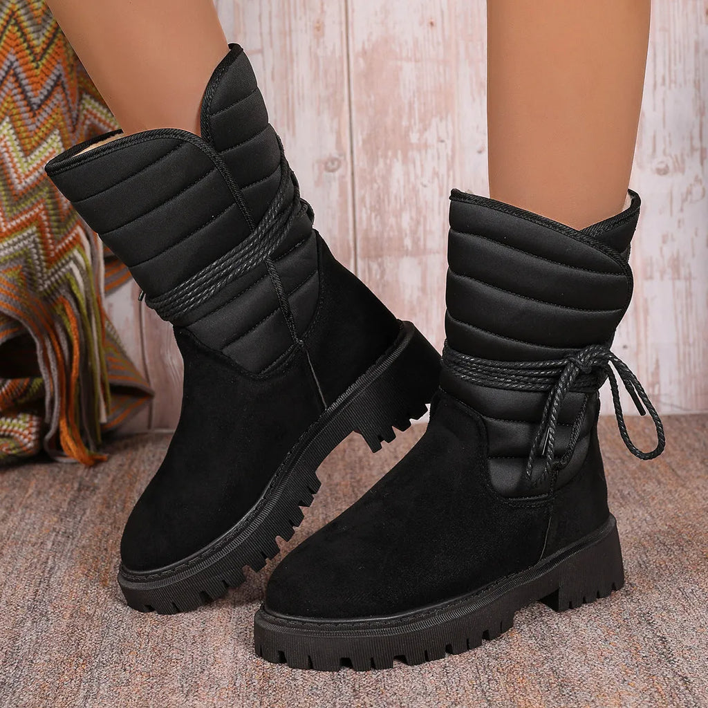 Women's black chunky heel snow boots with suede upper, rubber sole, and lace-up design on wooden floor
