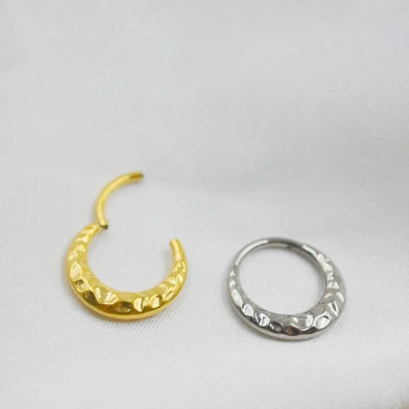 Titanium alloy concave-convex carved nose ring in gold and silver colours on a plain background.