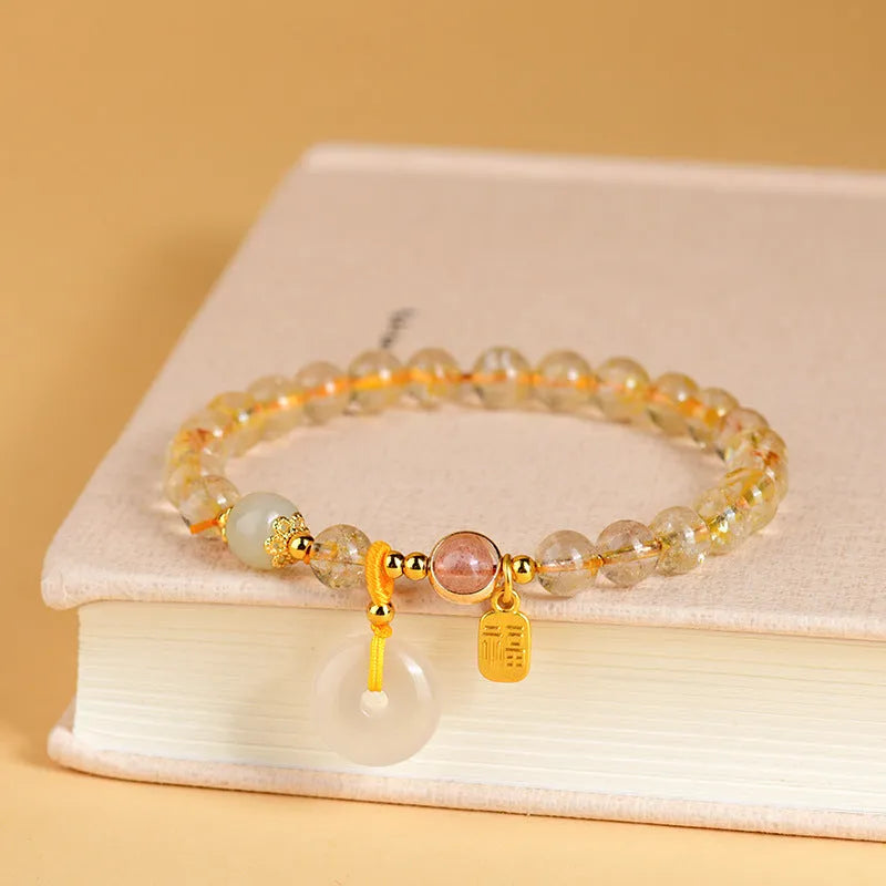 Gold rutilated quartz crystal bracelet with a safety buckle and a small rectangular blessing card pendant.