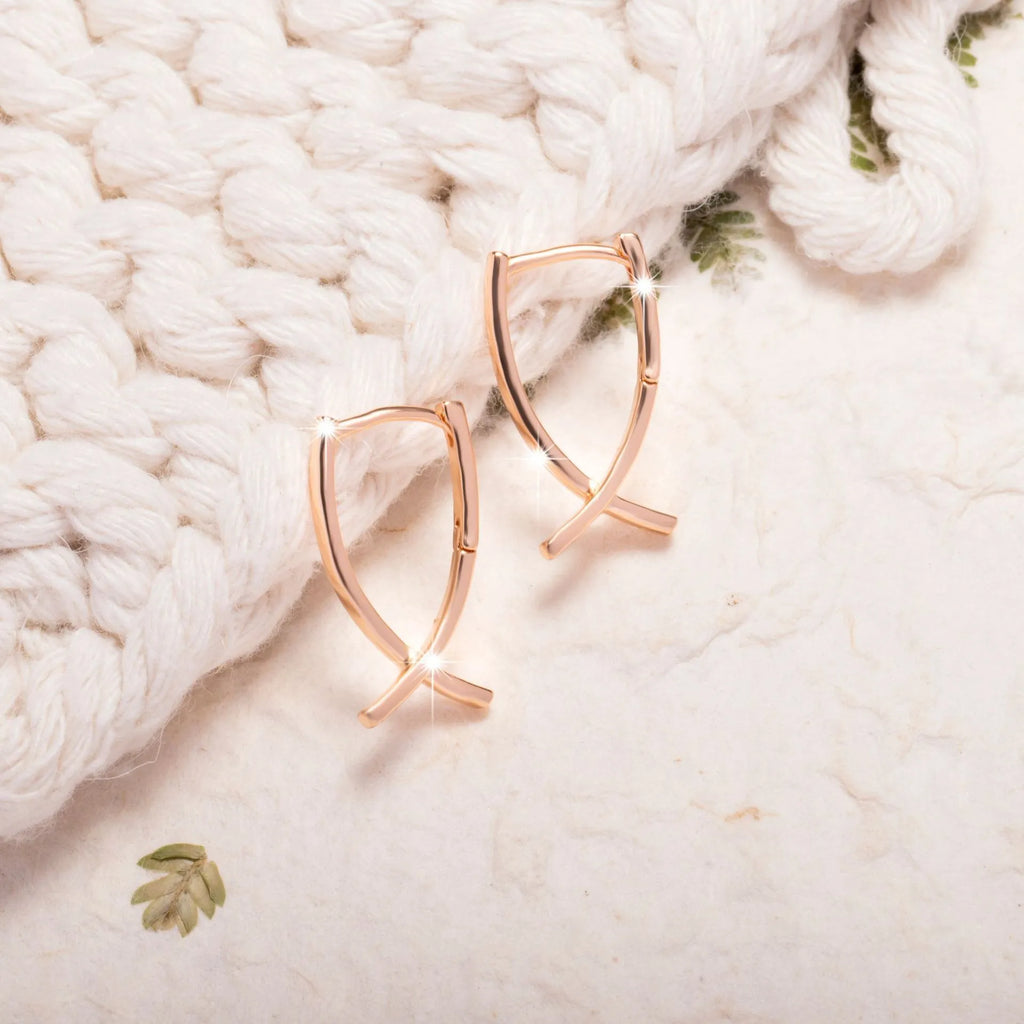 Pair of rose gold cross-shaped earrings on a plain background, showing pierced post design.