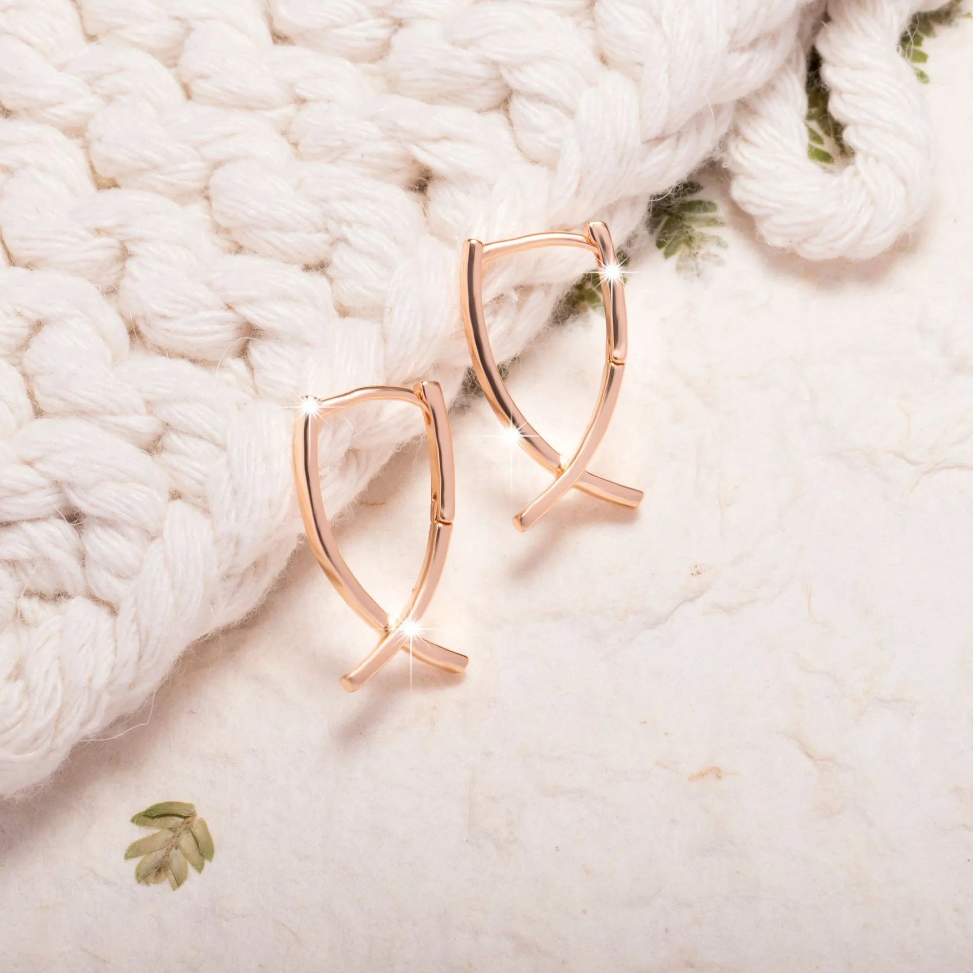 Pair of rose gold cross-shaped earrings on a plain background, showing pierced post design.