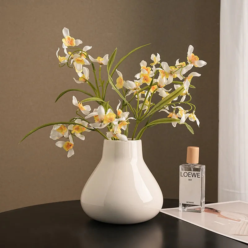 Black ceramic round belly vase with coloured glaze finish and two white orchid flowers displayed on wooden surface