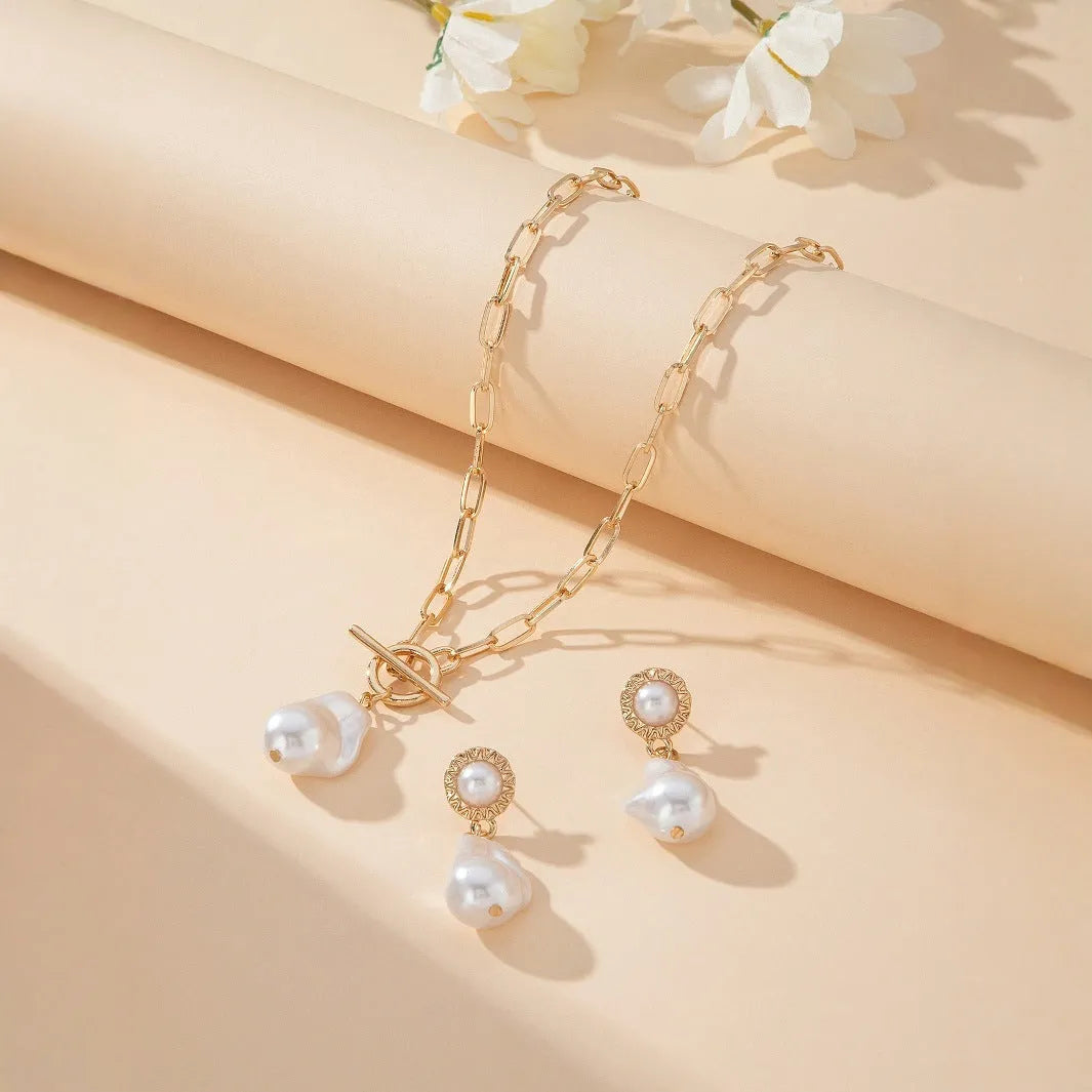 Gold-coloured iron necklace and earrings set with baroque pearl decorative elements on dark background