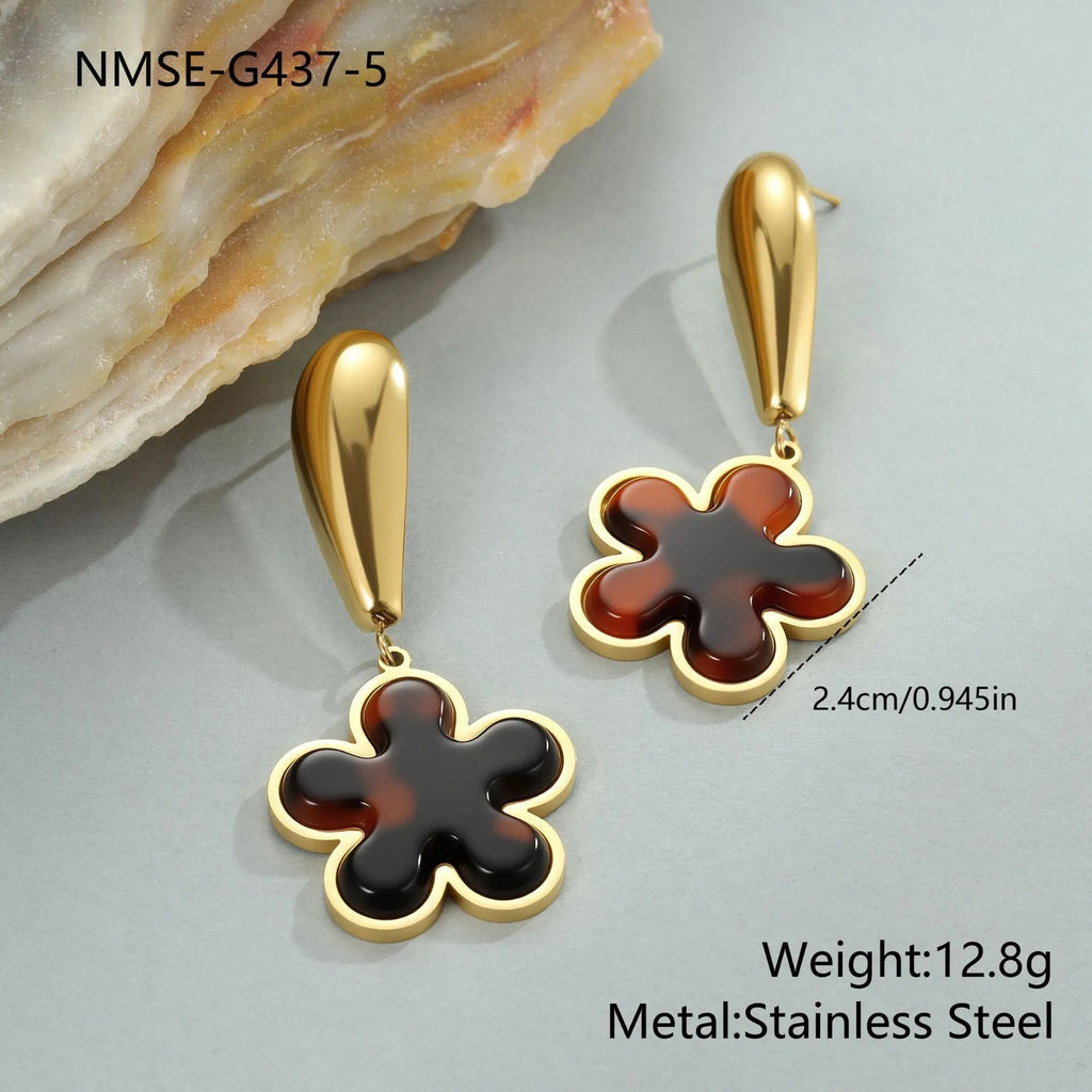 A pair of women's tortoiseshell resin earrings in hawksbill colour, showing heart-shaped and geometric flower designs on stainless steel with 18K plating.