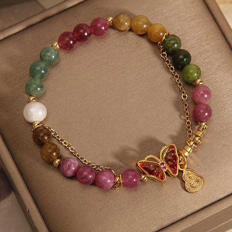 Close-up of a women's agate and tourmaline charm bracelet with butterfly and gourd shapes on a white background.