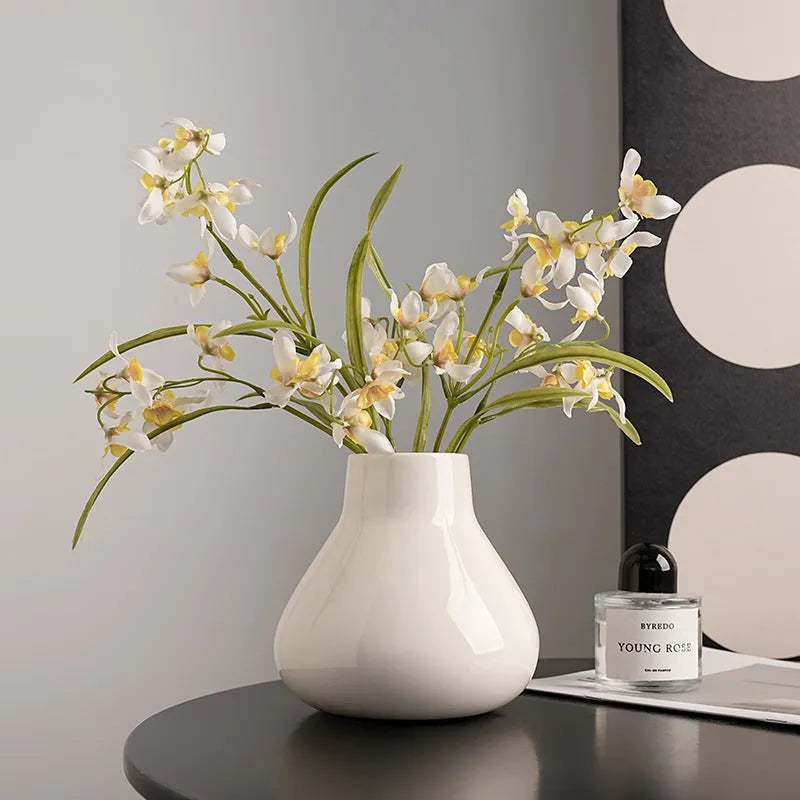 Black ceramic round belly vase with coloured glaze finish and two white orchid flowers displayed on wooden surface
