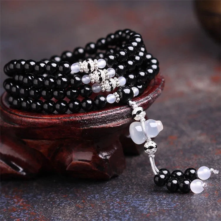 Black agate bracelet with 108 beads and geometric shape on a wrist.