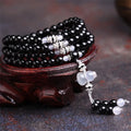Black agate bracelet with 108 beads and geometric shape on a wrist.