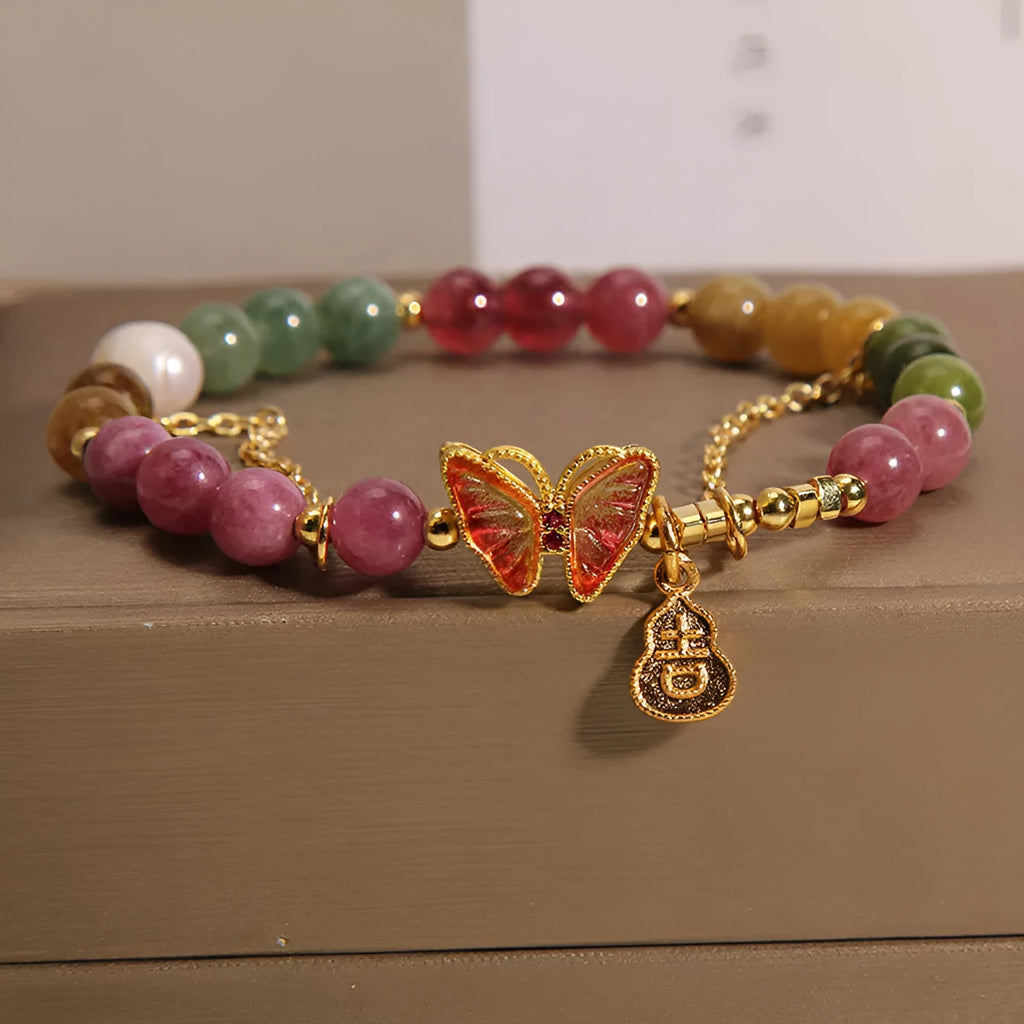 Close-up of a women's agate and tourmaline charm bracelet with butterfly and gourd shapes on a white background.