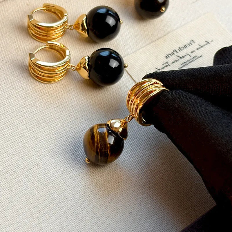 A pair of geometric tigereye stone earrings with 18K gold plating, showing natural brown bands, on a grey background.