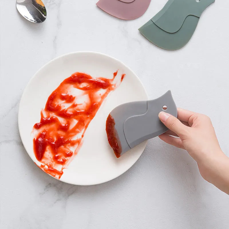 Green penguin-shaped kitchen scraper with soft blade, 11cm by 7cm, for cleaning plates and pots
