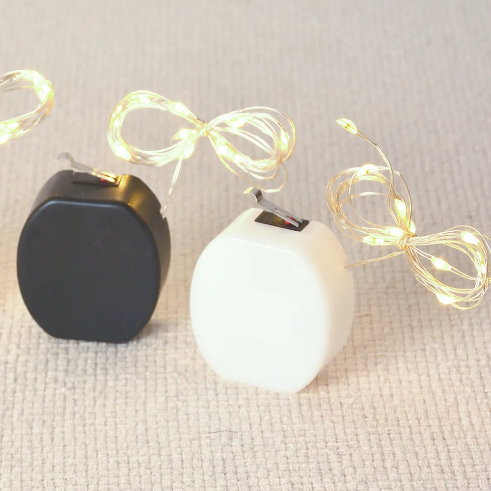 Close-up of a flexible copper wire LED light string with 20 small white LEDs and a white plastic CR2032 battery box.