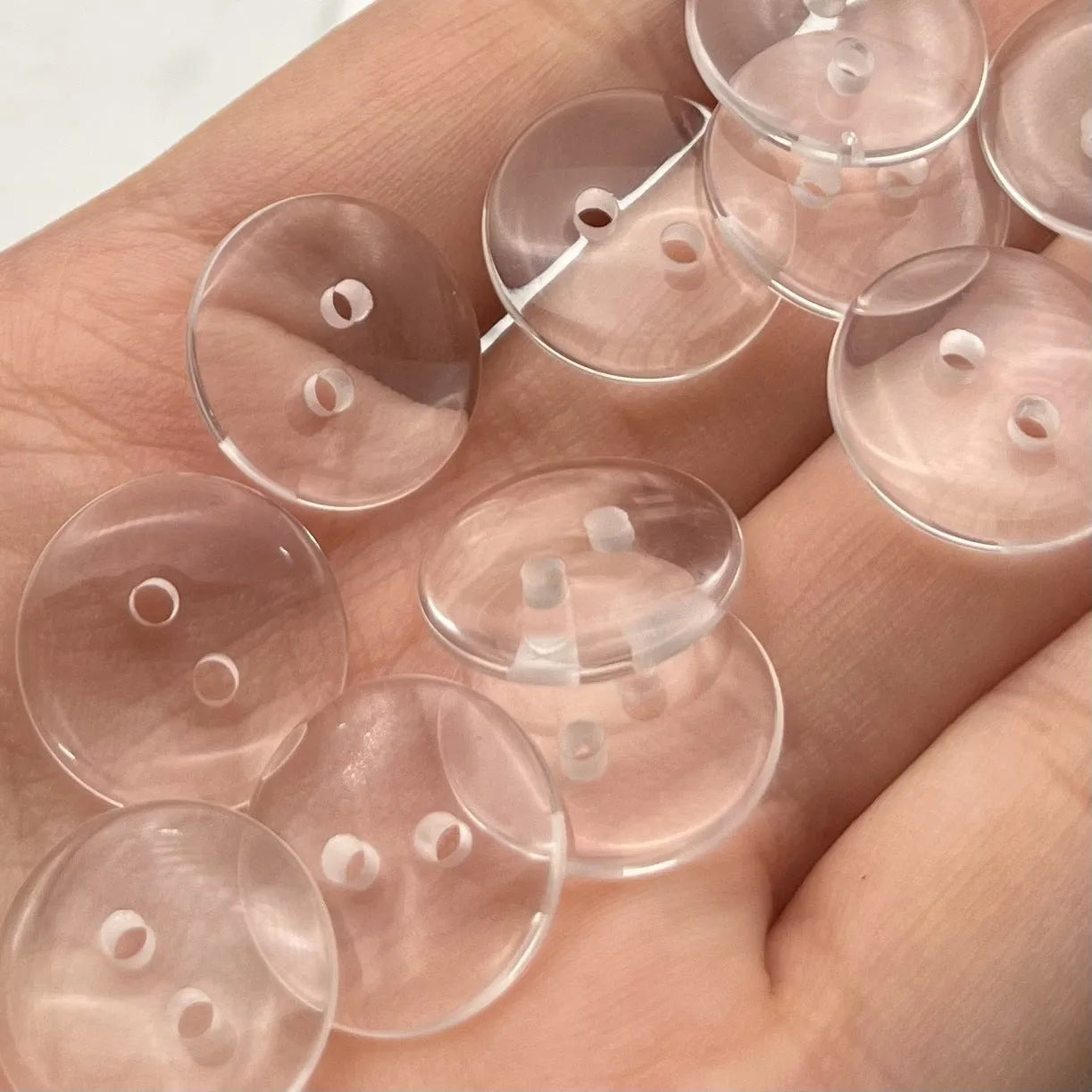 Close-up of a transparent, two-hole resin sewing button measuring 10mm in diameter.