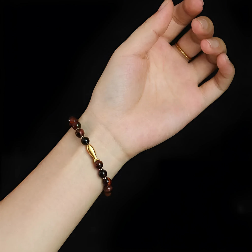 Yellow tiger eye bracelet with small fish bead charm on woman's wrist