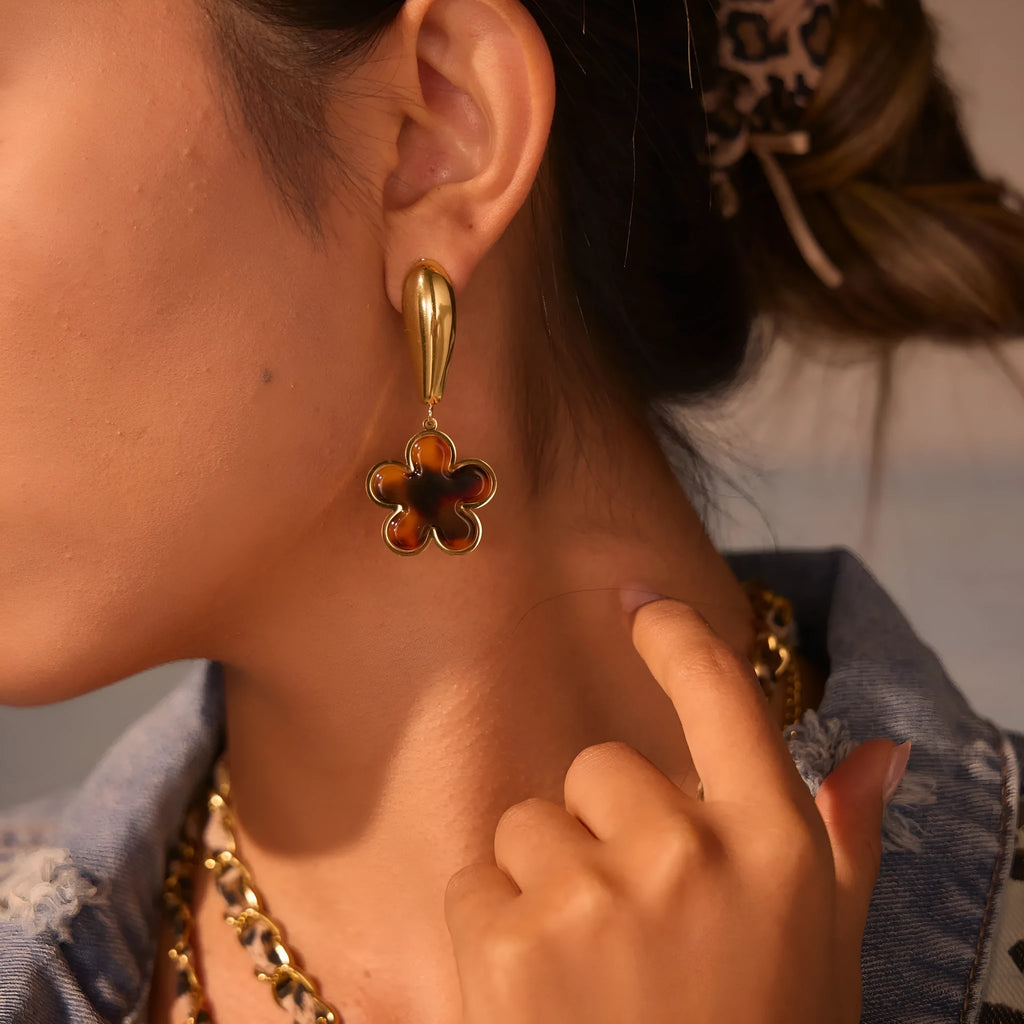 A pair of women's tortoiseshell resin earrings in hawksbill colour, showing heart-shaped and geometric flower designs on stainless steel with 18K plating.