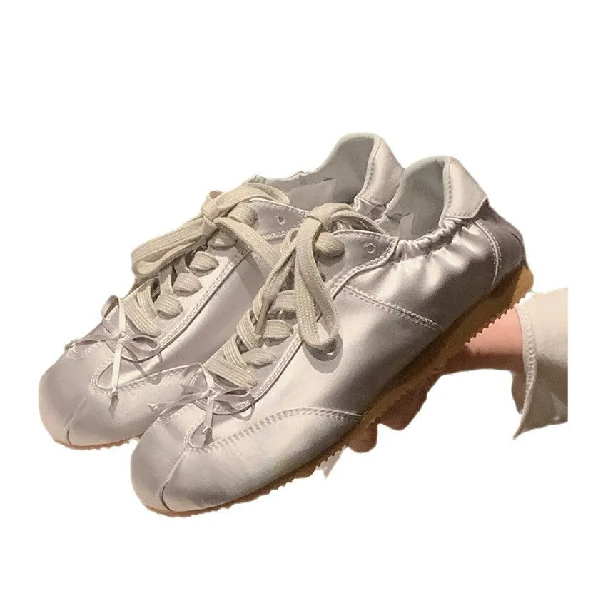 Women's silver grey satin ballet flat with front lace-up fastening and a round toe, shown on a white background.