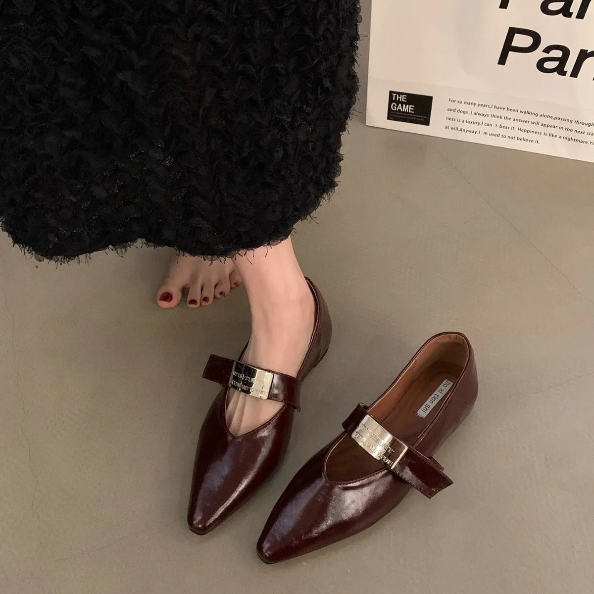 Women's black pointed toe Mary Jane shoes with a silver buckle and a low flat heel.