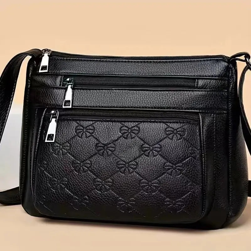 Women's black messenger bag with crossbody strap showing embossed detailing and exterior slit pocket
