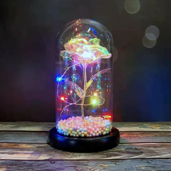 Gold artificial roses inside a clear glass dome ornament with LED lights and decorative accessories.