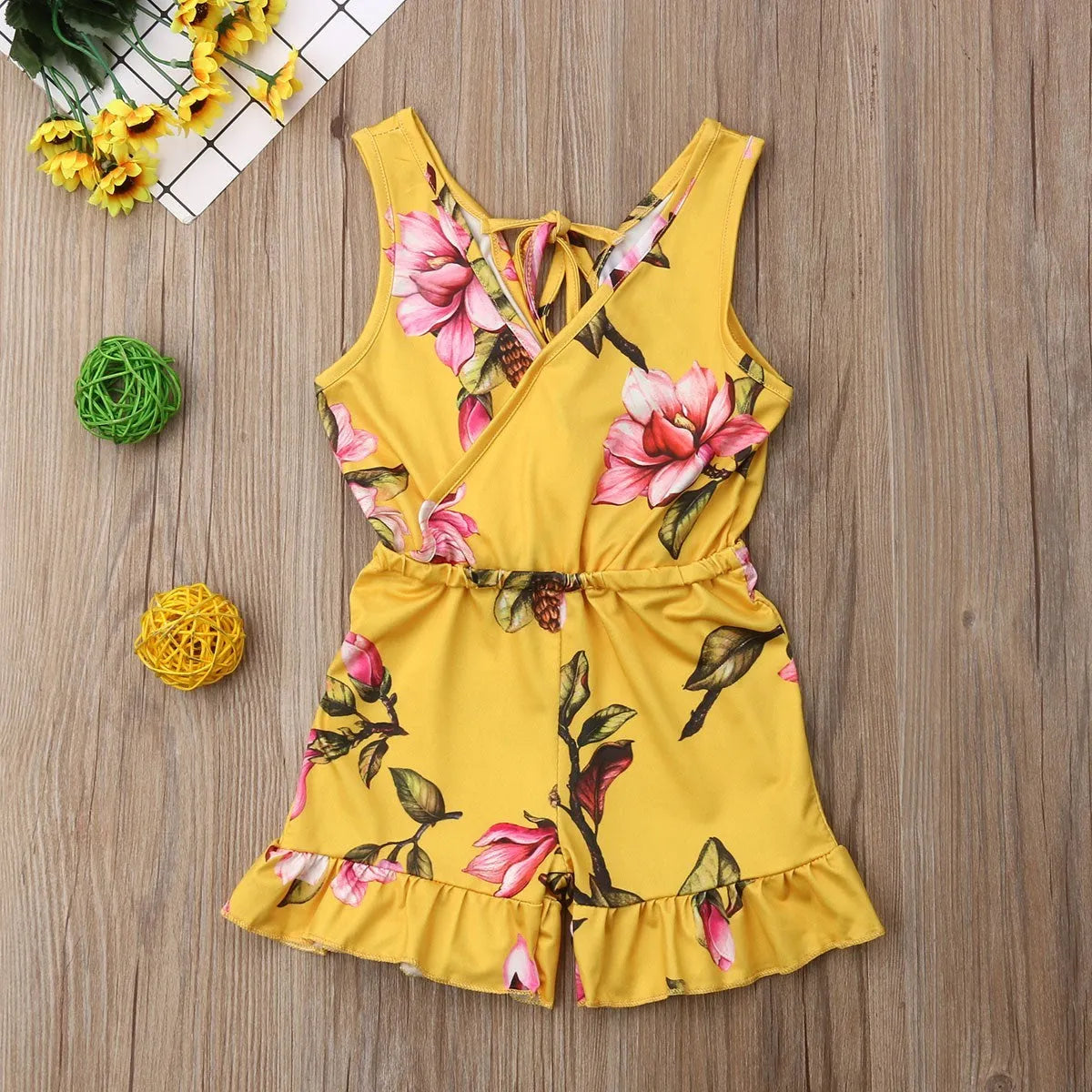 Baby girl wearing a white cotton floral romper suit with ruffle sleeves and bloomer-style bottom.