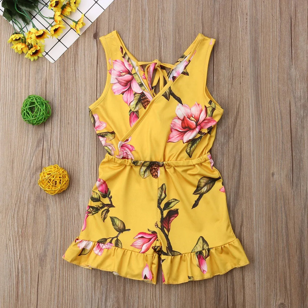 Baby girl wearing a white cotton floral romper suit with ruffle sleeves and bloomer-style bottom.