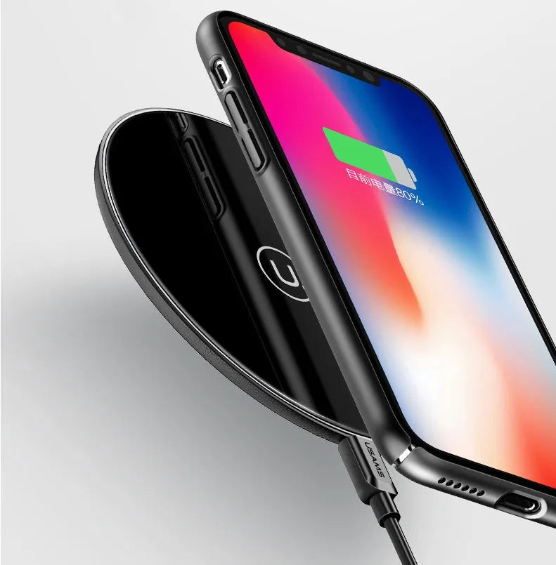 Black and white glass disc wireless charging pad for mobile phones on a wooden table.