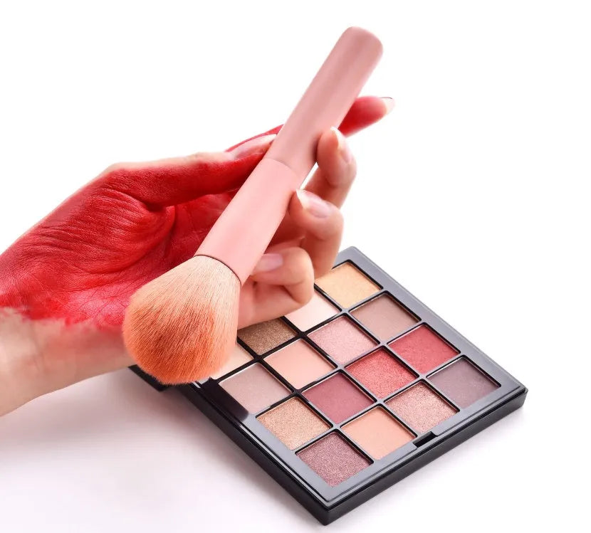 10 cosmetic brushes with wooden handles and nylon bristles arranged with makeup products