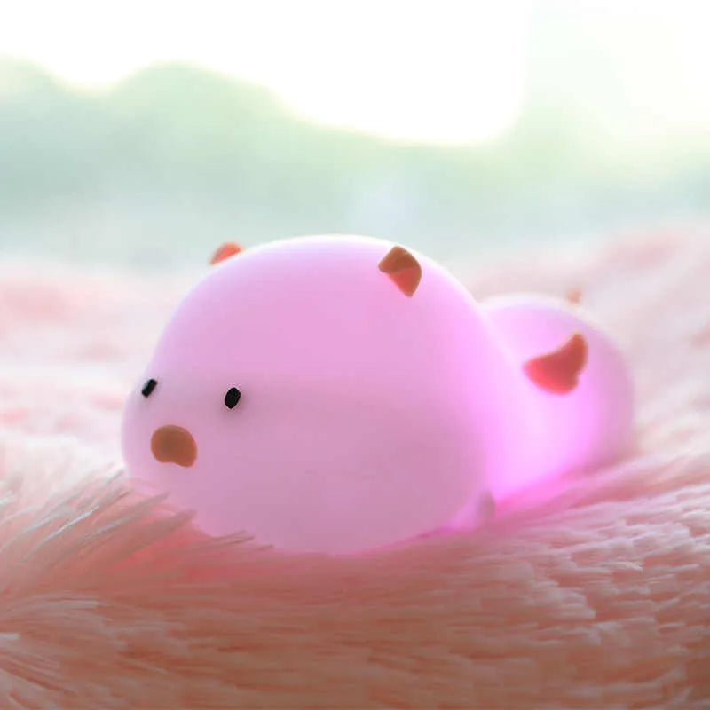 Cute pink silicone pig night light with sleeping design on a bedside table.