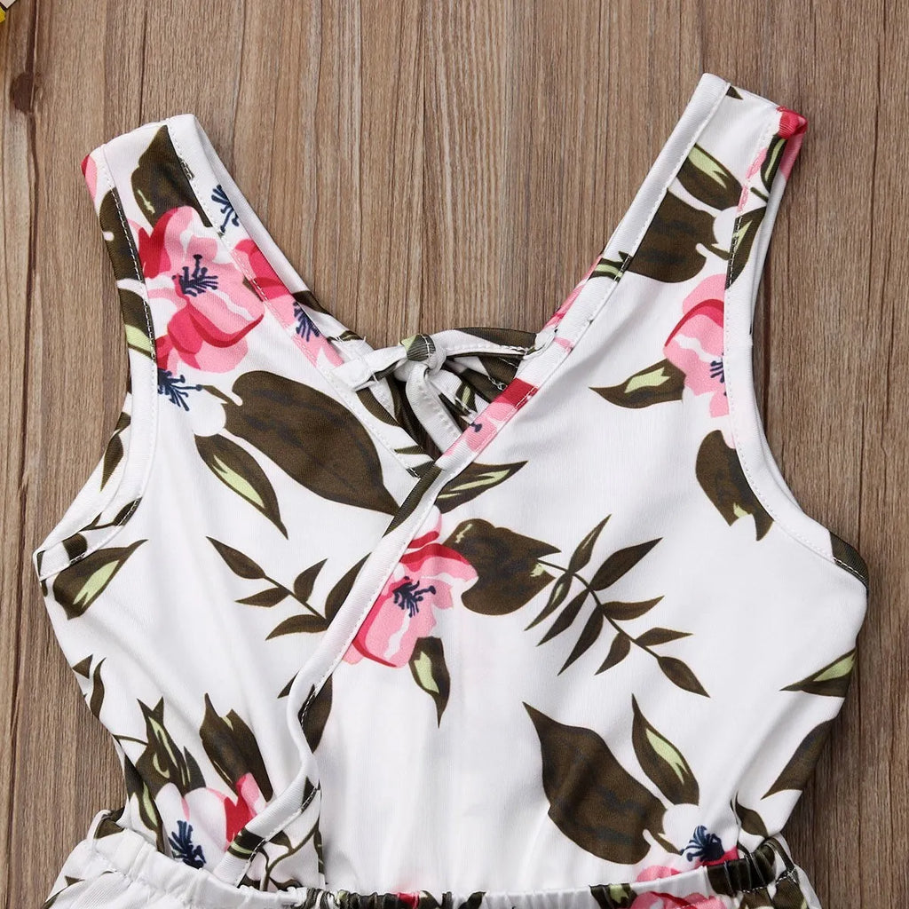 Baby girl wearing a white cotton floral romper suit with ruffle sleeves and bloomer-style bottom.