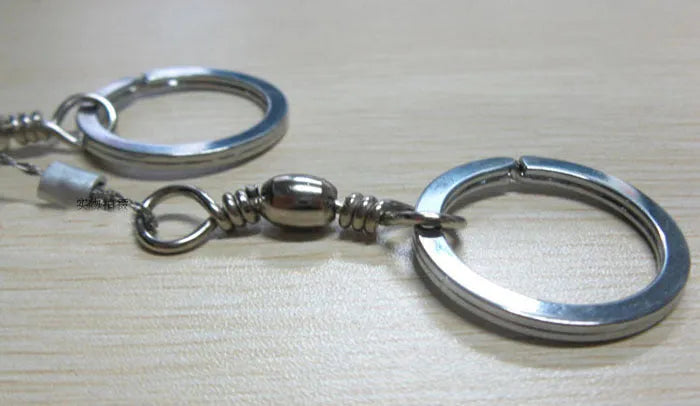 Coiled stainless steel survival wire saw with two black thumb rings, shown next to a ruler showing its 55cm length.