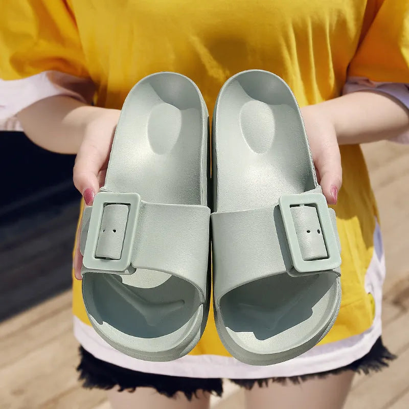 Women's grey blue buckle flip-flop slippers on a light background, showing adjustable strap and cushioned sole.