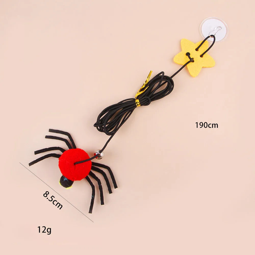 Red and yellow elastic rope cat toy hanging from a door, with feathers, a plastic spider, and a bell.