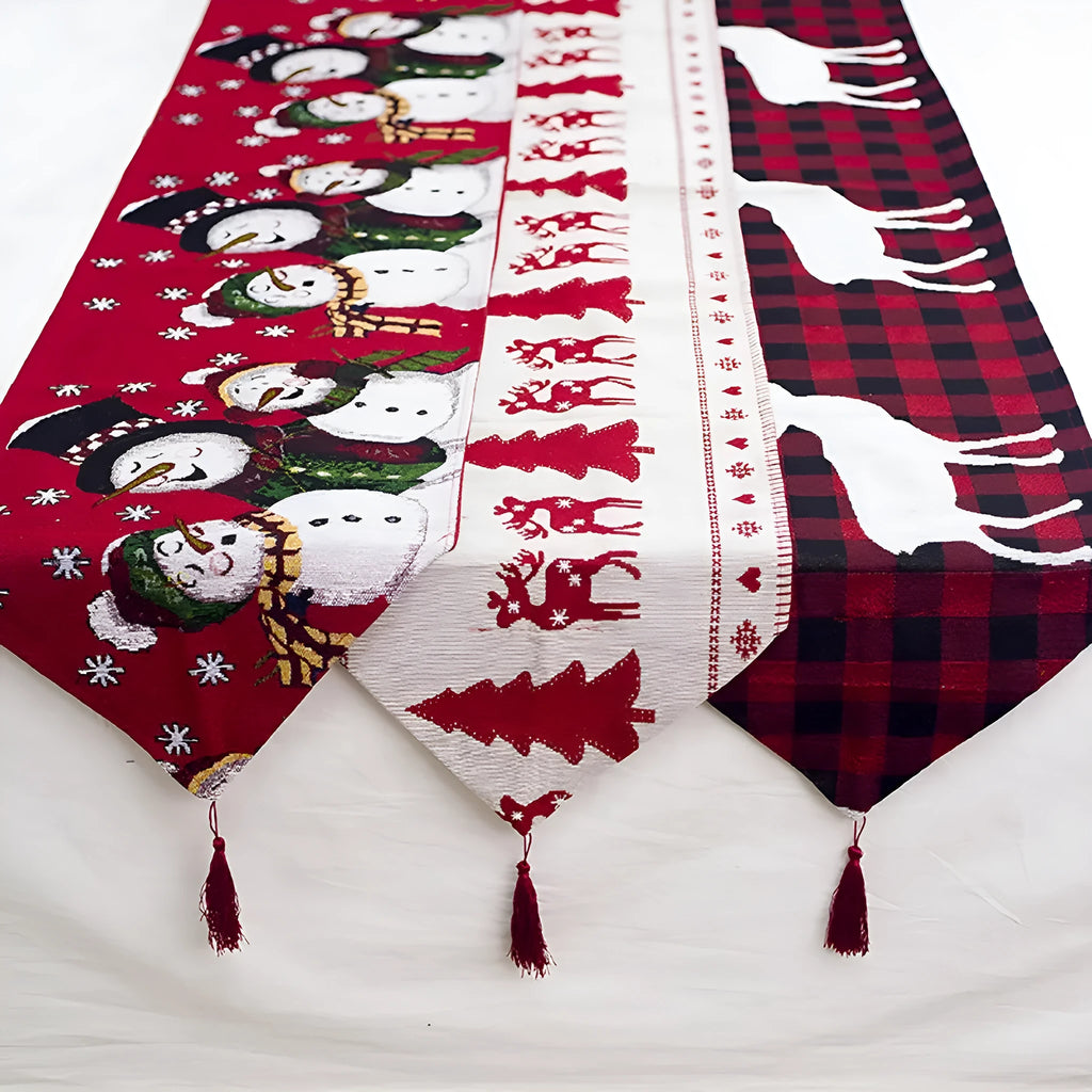 Red, white, and green Christmas table runner with elk and snowman print on a wooden dining table.