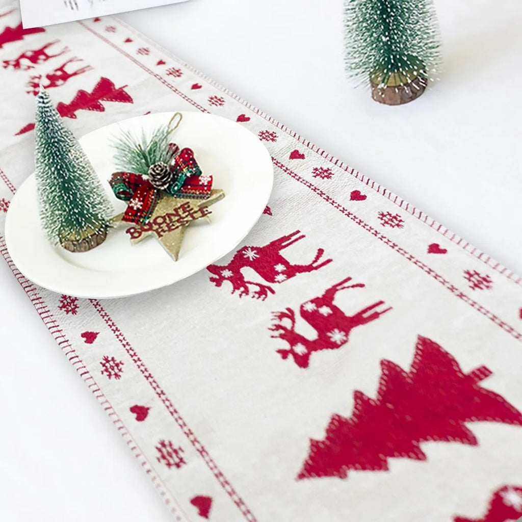 Red, white, and green Christmas table runner with elk and snowman print on a wooden dining table.