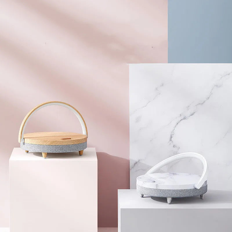 White marble-pattern wireless charging LED night light with built-in Bluetooth speaker and phone holder on wooden table.