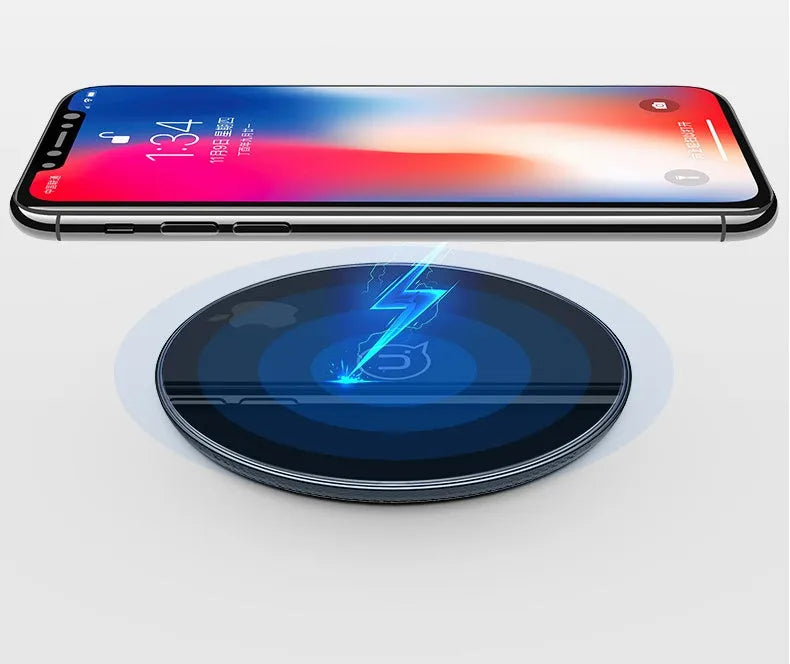 Black and white glass disc wireless charging pad for mobile phones on a wooden table.