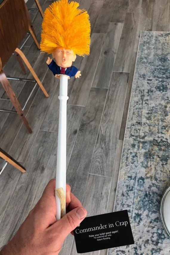 Yellow plastic Trump novelty toilet brush with a hanging slot on the handle.