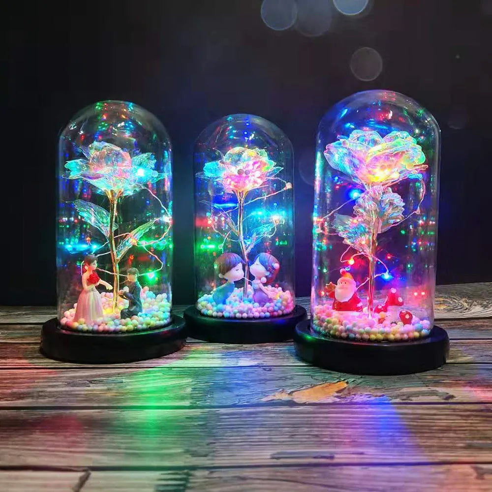 Gold artificial roses inside a clear glass dome ornament with LED lights and decorative accessories.