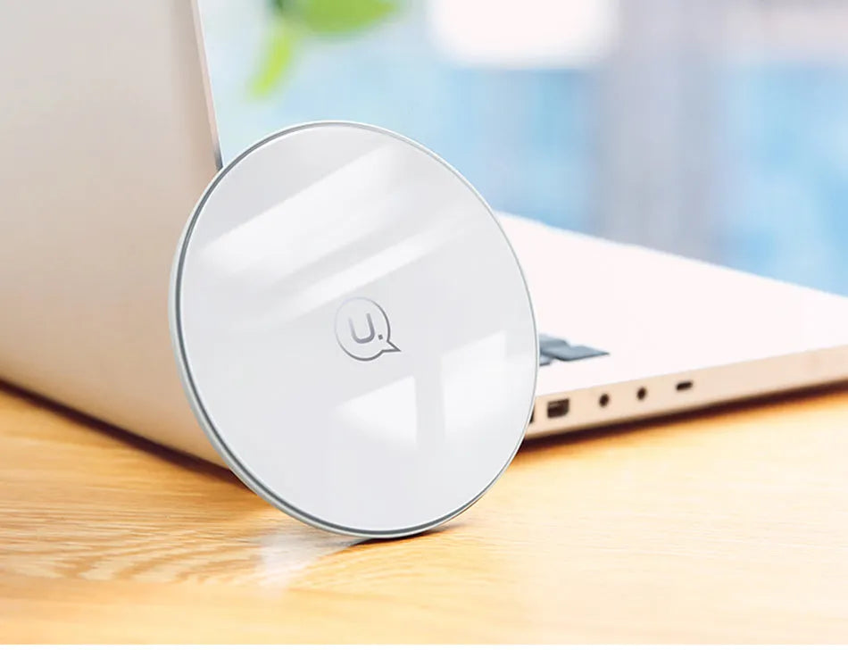 Black and white glass disc wireless charging pad for mobile phones on a wooden table.