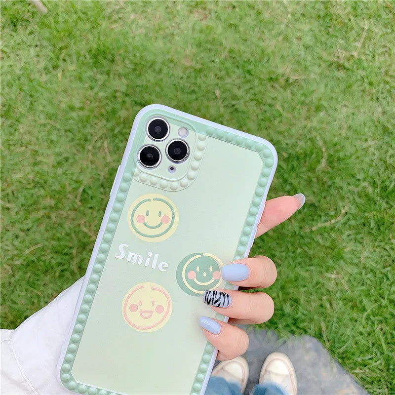 Green TPU iPhone case with geometric smiley face and polka dot frame designs on a table