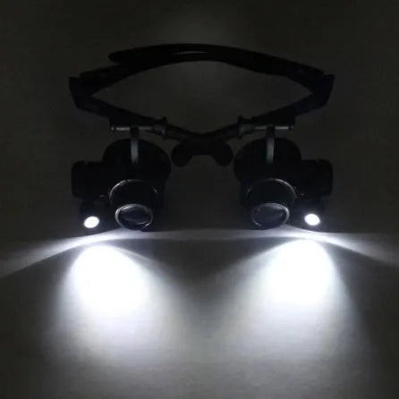Black hands-free magnifier glasses with LED lights and four pairs of interchangeable magnification lenses on a workbench.