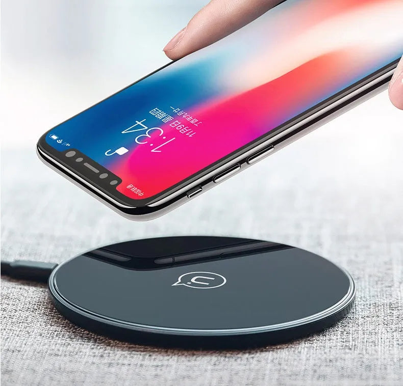 Black and white glass disc wireless charging pad for mobile phones on a wooden table.