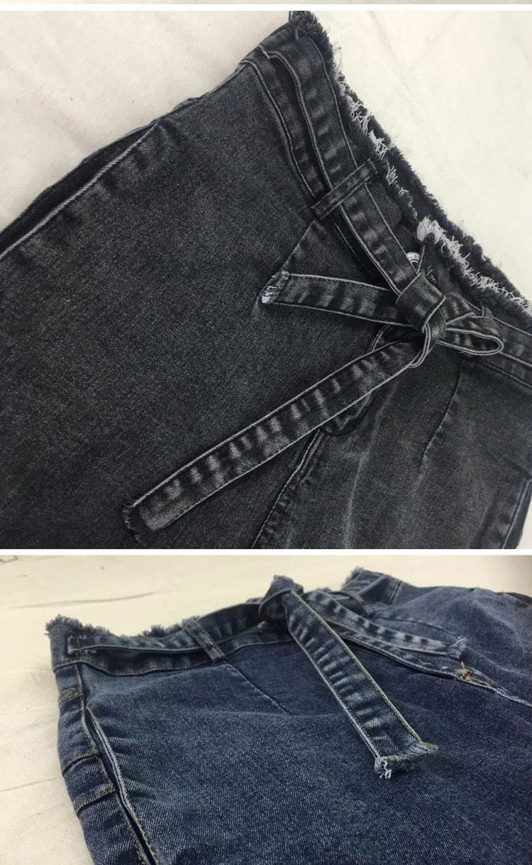 A pair of light blue fringed jeans with a distressed hem laid flat.