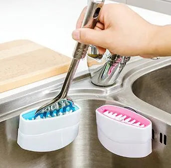 Coloured kitchen brush with knife and fork design and a white suction cup on its handle.