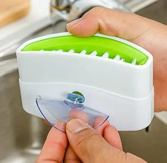 Coloured kitchen brush with knife and fork design and a white suction cup on its handle.
