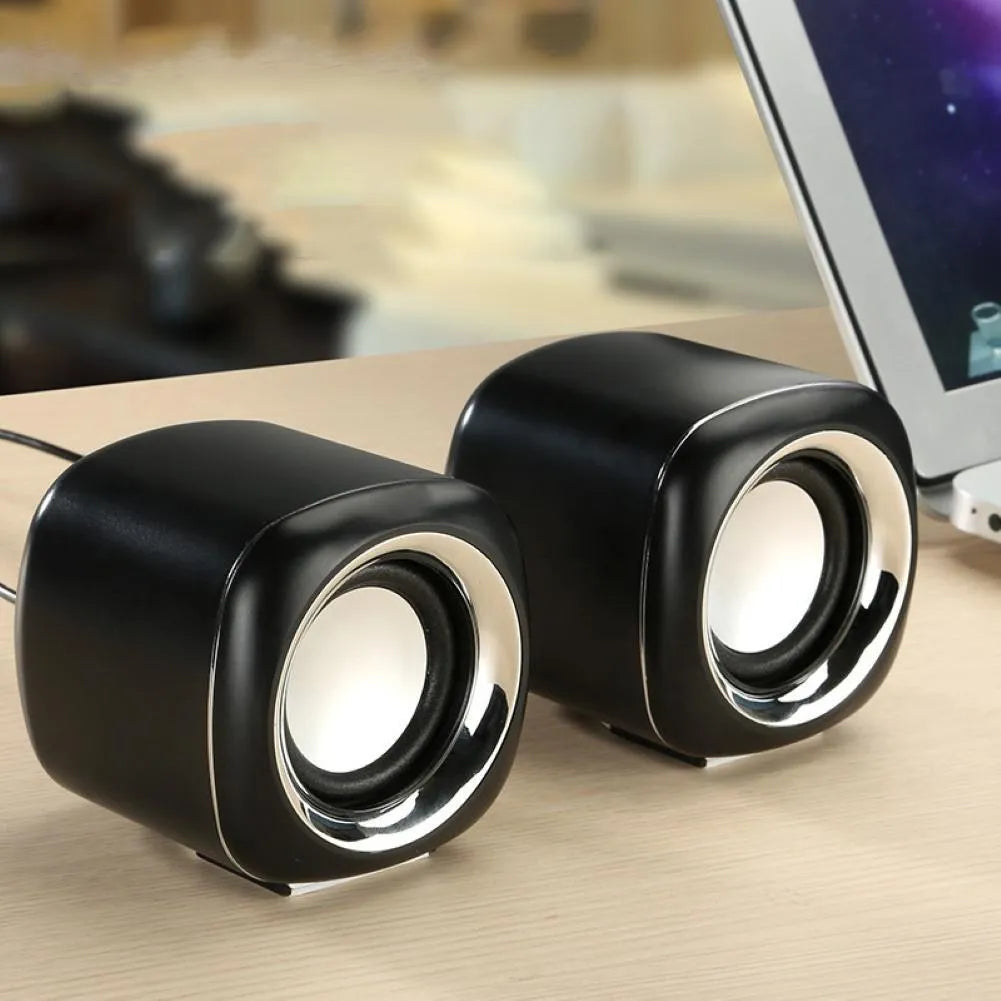 Pair of black wired mini desktop speakers with 3.5mm plug, showing compact cubic shape.
