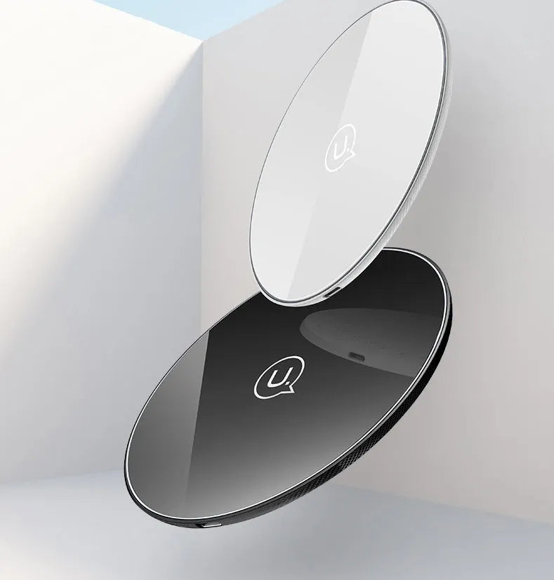Black and white glass disc wireless charging pad for mobile phones on a wooden table.