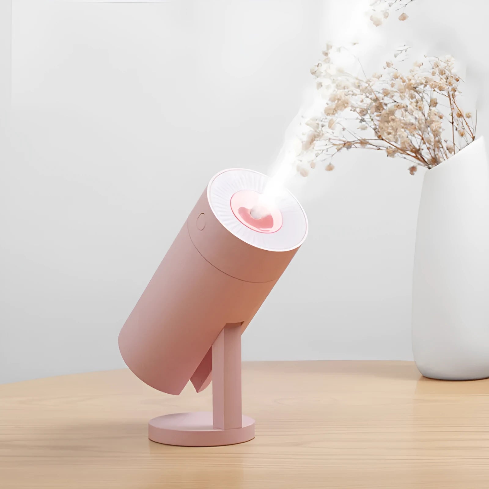 A compact white folding bracket USB humidifier on a desktop next to a laptop, showing its mist output.